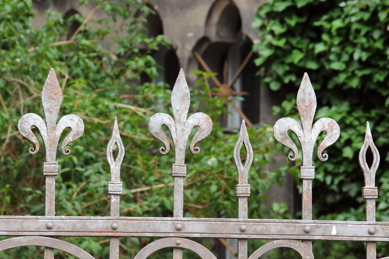 White ornamental iron fence with spear-point finials in front of greenery